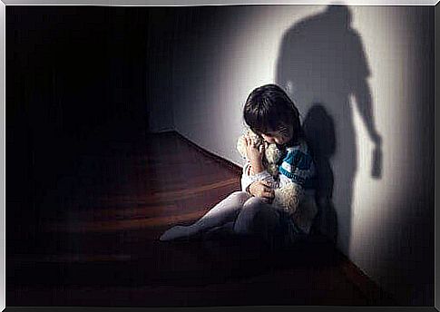 Child hugs teddy bear with shadow of man in front of him